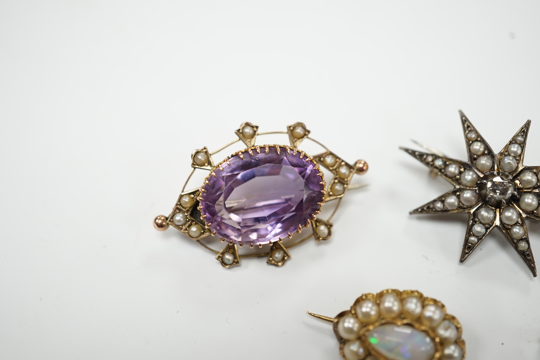 An early 20th century 9ct, amethyst and seed pearl set oval brooch, 33mm, a yellow metal and seed pearl set crescent brooch, a yellow metal, opal and split pearl set brooch and a rose cut diamond and split pearl set star